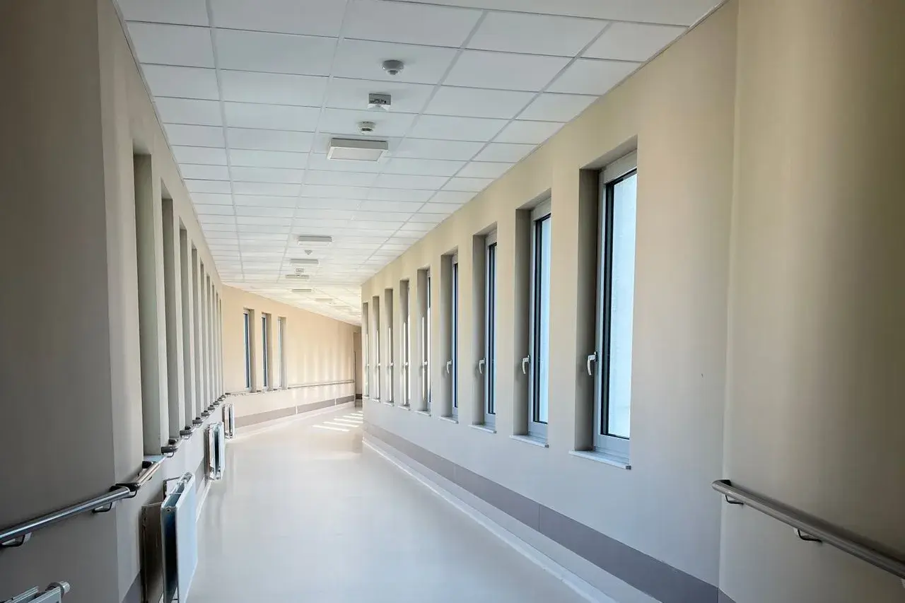 Büyük pencereli, tutamaklı, aydınlık ve boş bir hastane koridoru